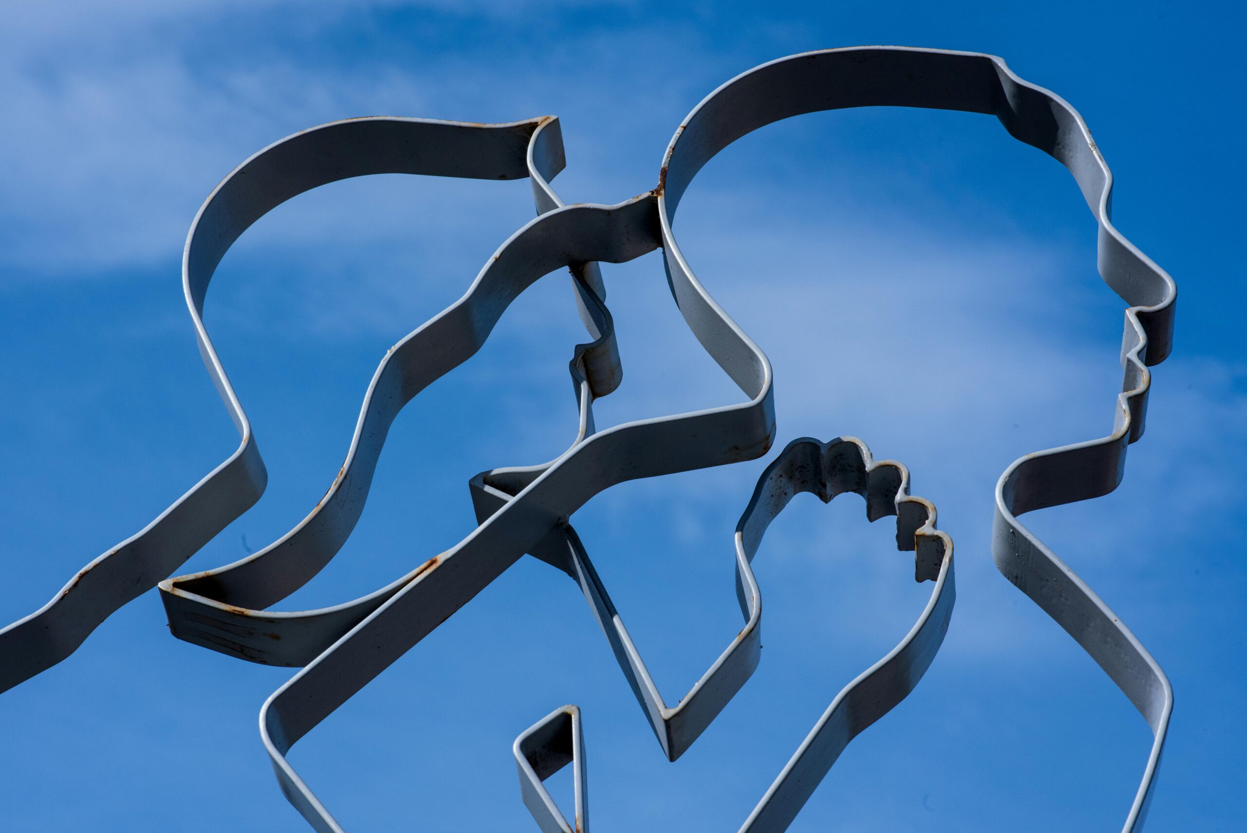 Abstrakte metallische Silhouettenskulptur mit blauem Himmelshintergrund.